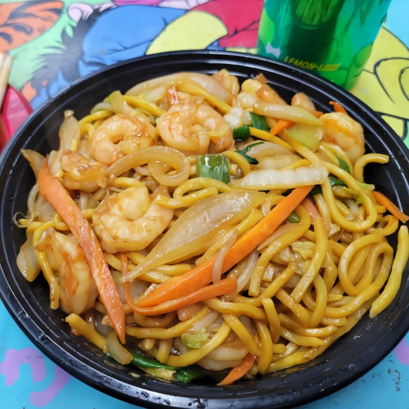 Shrimp lo mein with noodles, carrots, onions, and green onions in a black bowl.