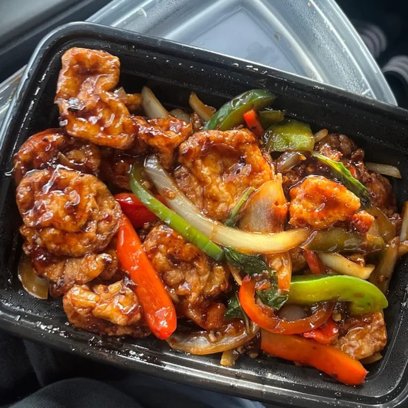 Bite of Asia's sweet and sour chicken with bell peppers and onions in a black takeout container.