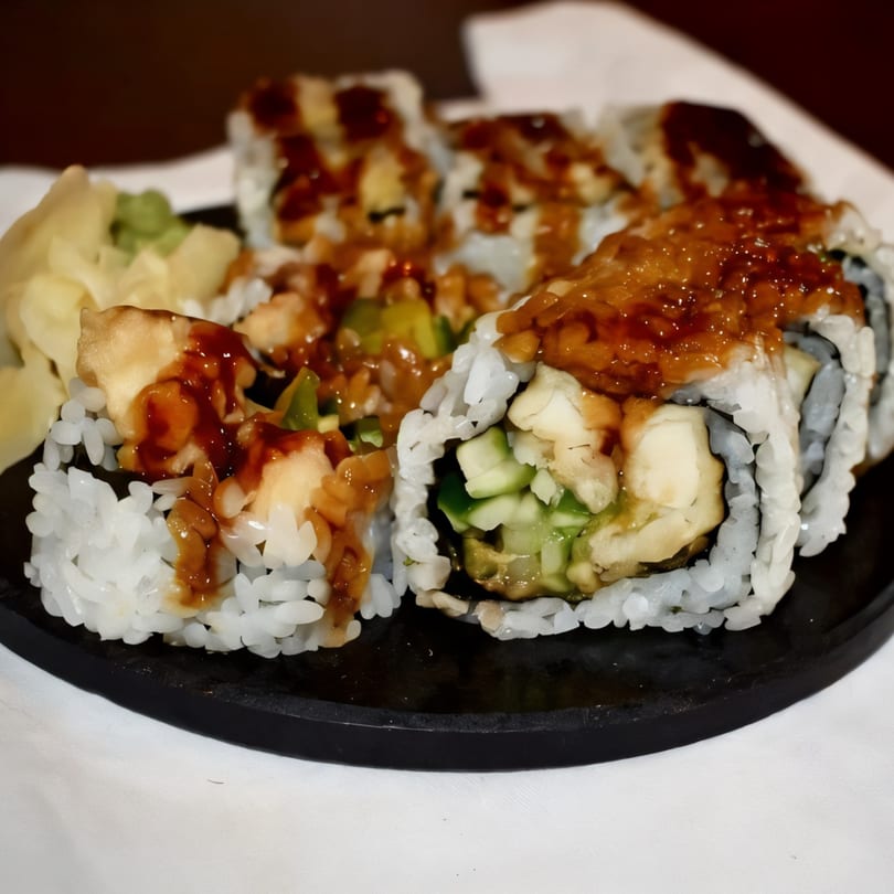 Sushi rolls with white rice, green vegetables, and a dark sauce, served with pickled ginger.